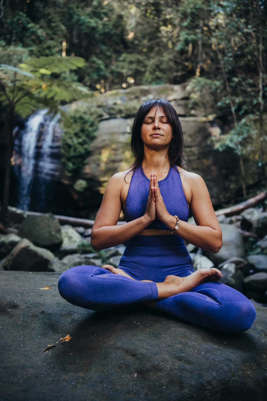 Woman meditating beside a waterfall